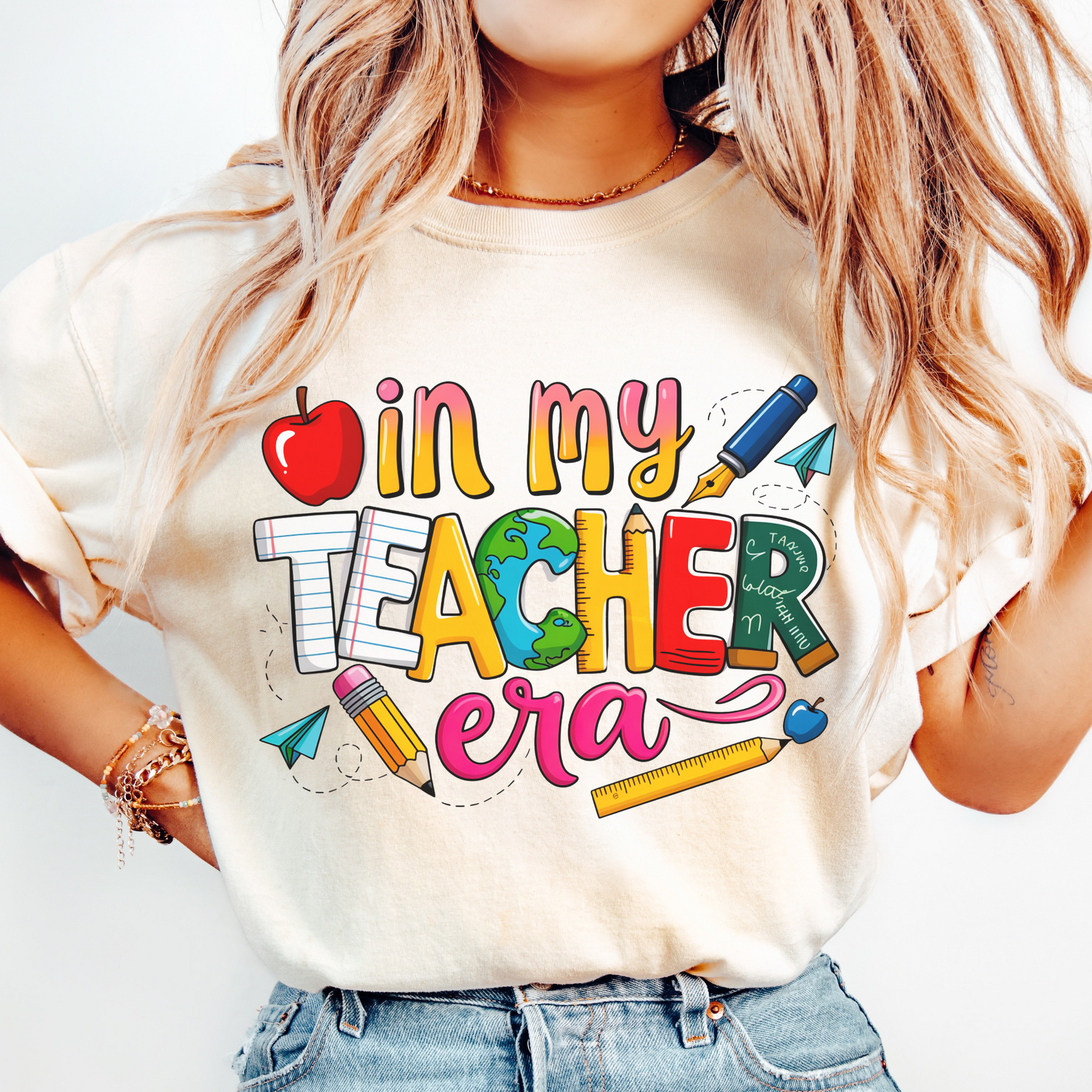 Person wearing a white t-shirt with colorful text and graphics, including an apple, pencil, and ruler.