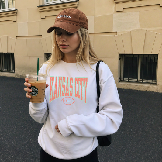 Woman wearing a 'Kansas City' sweatshirt holding a Starbucks drink outdoors.
