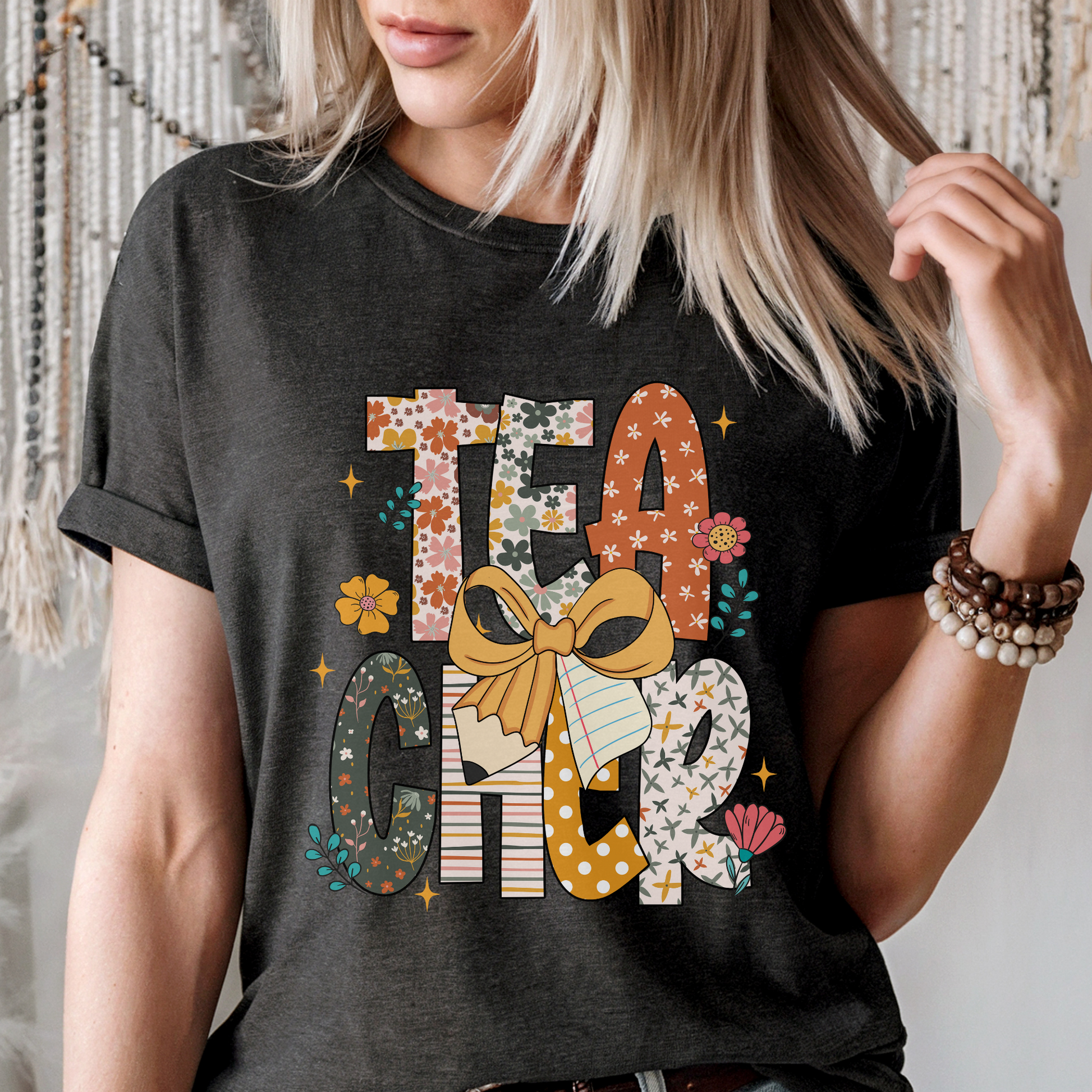 Person wearing a black t-shirt with TEACHER design featuring a bow and floral elements.