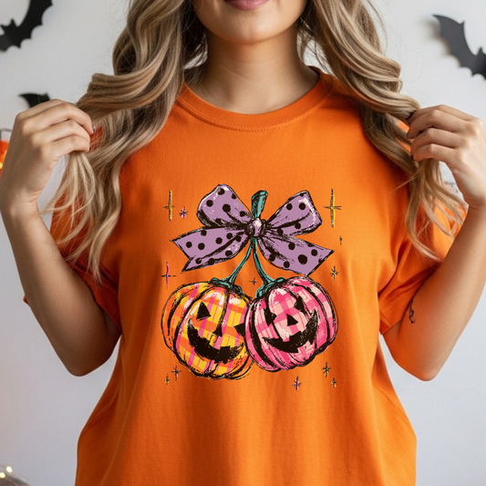 Person wearing an orange t-shirt with Halloween-themed design of pumpkins and a bow.