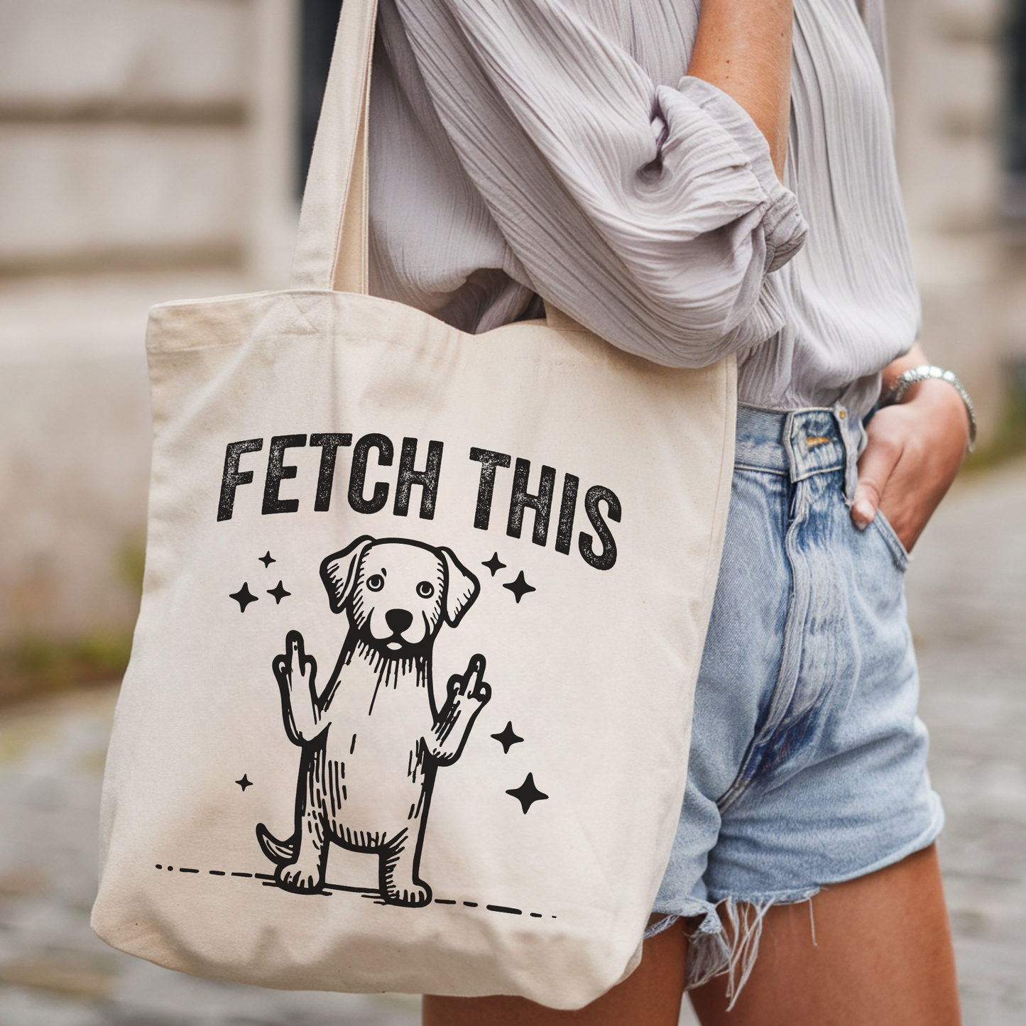 Person holding a tote bag with a dog graphic and 'FETCH THIS' text.